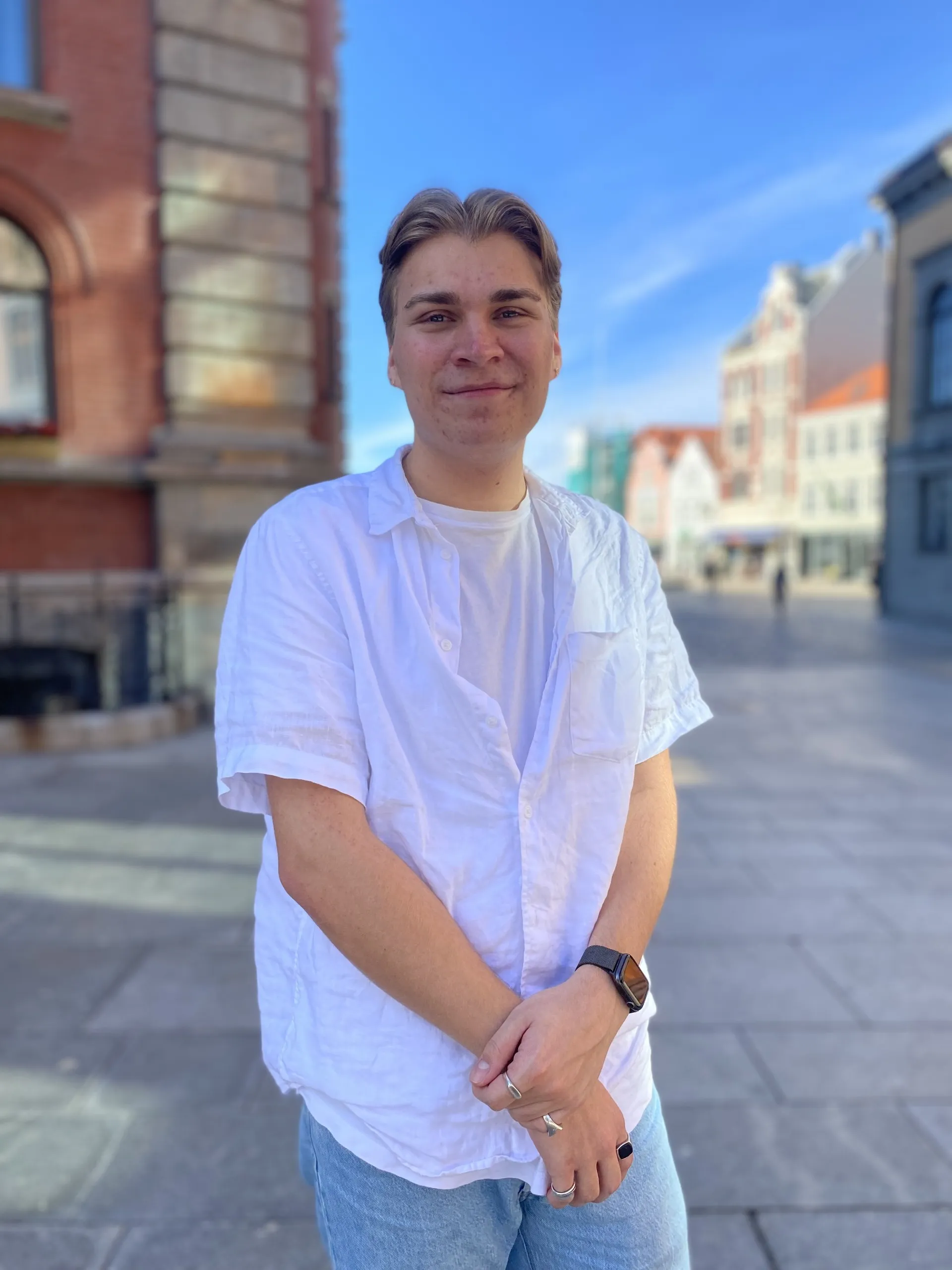 Eirik Helgesen i hvit skjorte, smilende foran gamle bygårder.